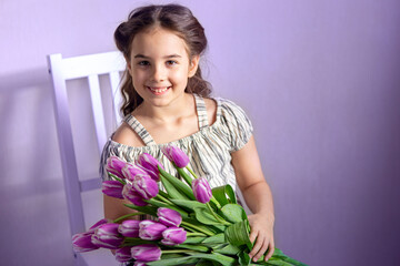 Beautiful little girl with a bouquet of tulips, against the background of a purple wall