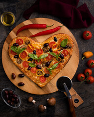 Wooden board with homemade  heart-shaped pizza with ingredients on black background. Valentine's Day celebration.