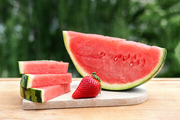 Strawberries and seedless watermelon slices on a cutting board outdoors, summer berry concept.