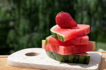 Watermelon slices and strawberries on cutting board outdoors.