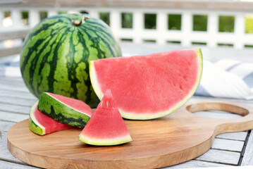 Watermelon and slices on a table on wooden terrace. - obrazy, fototapety, plakaty