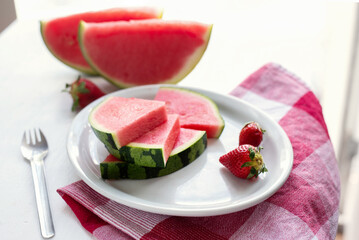 Watermelon slices and strawberries on a plate on a white table.