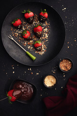 Dessert with chocolate covered strawberries on  black plate on  black background, top view.