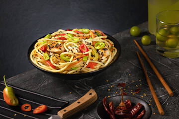 Stir fry noodles with vegetables and chicken in black wok pan. Dark background. Copy space.