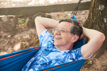 Hispanic senior man lying in a blue hammock laughing.