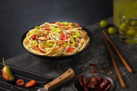Stir fry noodles with vegetables and chicken in black wok pan. Dark background. Copy space.