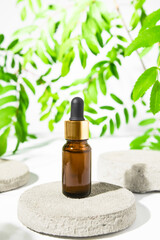 Brown glass bottle with serum, essential oil on a stone with beautiful plant leaves in the background, beauty product.