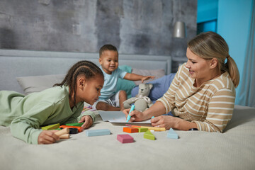 Portrait of happy Caucasian mother with two African American children playing on bed together - Powered by Adobe