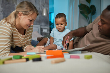 Naklejka premium Portrait of multiethnic family with cute baby boy playing together while lying on bed at home