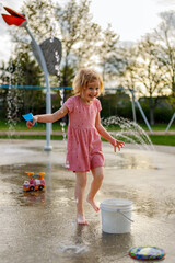 Naklejka premium Happy child playing at splash pad playground in summer. Water park with fountains for children