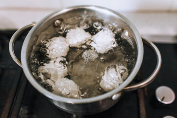 Chicken white eggs are boiled in boiling water in a metal pan on the stove. Morning breakfast, food photography.