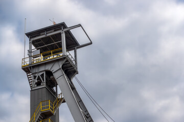 View of the mine shaft elevator wheels against the cloudy sky. The object is lit by natural sunlight passing through the clouds
