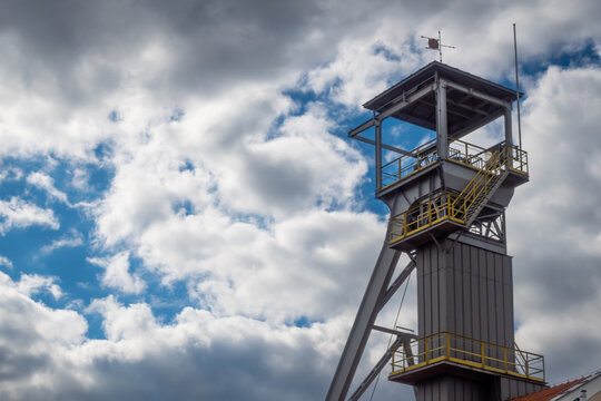 View of the mine shaft elevator wheels against the cloudy sky. The object is lit by natural sunlight passing through the clouds