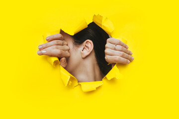 Female ear and two hands close-up. Copy space. Torn paper, yellow background. The concept of...