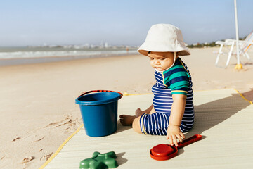 Portrait of a baby boy sitting on the beach during summer vacation at sea