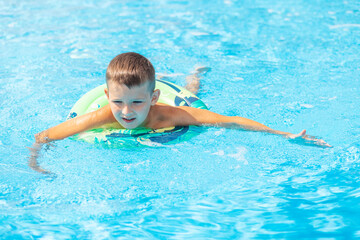 Fototapeta na wymiar Funny happy child boy in swiming pool on inflatable rubber circle ring. Kid playing in pool. Summer holidays and vacation concept