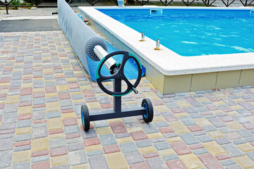 Blue tarpaulin pool cover and mechanical reel. Bubble awning film for covering the pool. Pool with...