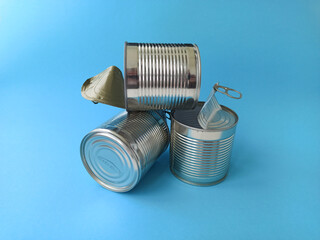 Two shiny metal cans from under canned food lie on a blue background. The concept of ecology, waste recycling and environmental conservation