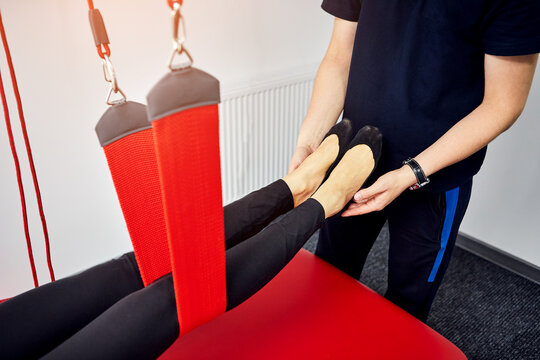 Rehabilitation specialist doing active treatment on suspension straps to female patient. Concept of therapeutic exercises to restore pain-free movement patterns and improve function