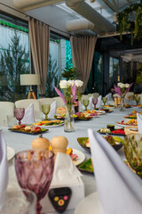 Festive table with appetizers. Salads, cheese and meat plates. Empty glasses, plates, chairs for guests. Vases with decorative flowers