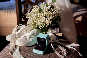 Bridal bouquet with satin ribbon, women shoes, veil and two golden wedding rings on chair, copy space. Wedding concept