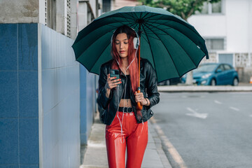 red-haired girl with mobile phone and headphones on the street with umbrella