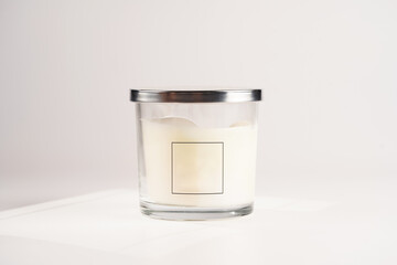 Blank off-white pillar candle in glass jar with label and silver colored lid on white background