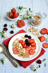 vertical composition. Oatmeal with muesli, strawberries and blackberries on a light wooden background