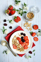 Top view of a plate with oatmeal with muesli, strawberries and blackberries on a light wooden background. Vertical