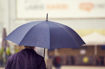 a man walking in the city with a black umbrella on a rainy and windy day.