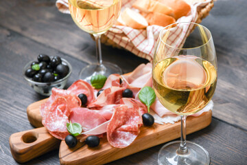 Food antipasto prosciutto ham, salami, olives and bread sticks. Charcuterie board. Two glasses of...