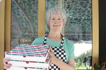 Senior pizzeria worker holding pizza boxes 