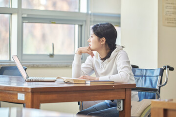 아시아 한국의 대학교 도서관에서 휠체어에 앉아서 책상위의 노트북과 책을 보고 있는 여자 모델