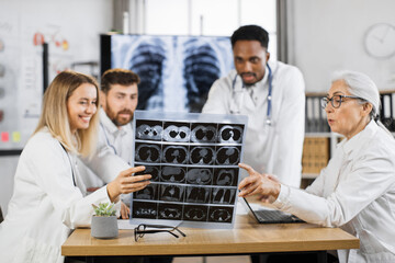 Multiracial male and female doctors having briefing at clinic for examination patient x ray scan. Team of coworkers in lab coats using various modern gadgets for work.