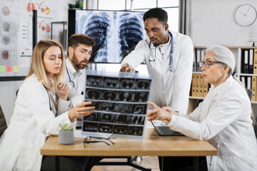 Fototapeta premium Multiracial male and female doctors having briefing at clinic for examination patient x ray scan. Team of coworkers in lab coats using various modern gadgets for work.
