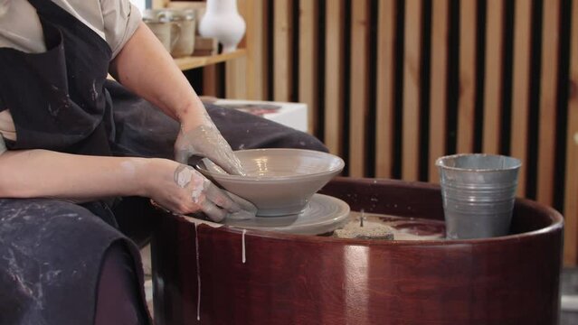 An elderly woman shaping a soup plate out of piece