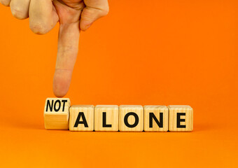 You are not alone symbol. Businessman turns wooden cubes and changes concept words alone to not alone. Beautiful orange background. Business, support and you are not alone concept. Copy space.