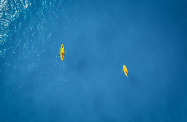 Aerial view of yellow kayaks in blue sea at sunset in summer. Man and woman on floating canoe in...