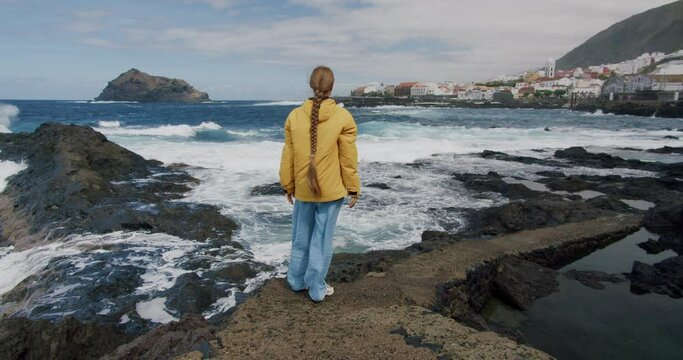 Young woman tourist enjoying the seaside. The girl carefree raiser her arms- Garachico. Tenerife. Canary Islands. Spain