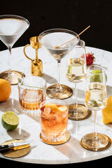 Negroni, martini cocktail (garnished with olive), Martinez (garnished with lavender) and Prosecco, on a carrara white marble table - obrazy, fototapety, plakaty