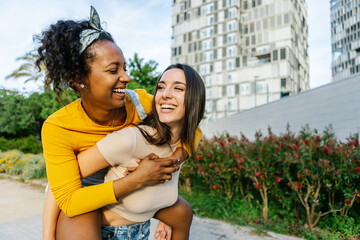 Couple of young women in love piggybacking in city street - Two best female friends having fun together outdoors