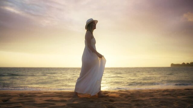 Young beautiful American woman in love getting married on ocean beach at cinematic golden sunset above horizon. Marriage, love, romance, summer vacation by sea RED 6K video. Lady in white boho dress 