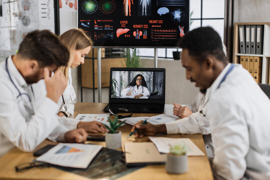 Medical Staff Receiving Plan For Week During Online Briefing With Female African American Physician Chief. Concentreted Worker Reading Work Recommendation While Sitting At Table In Medical Center.