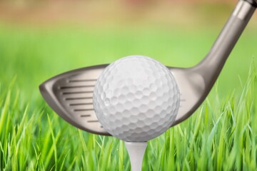 Golf club and ball on green grass ready to be struck on golf course background, evening time.