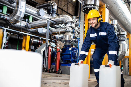 Petrochemical industrial worker carrying plastic canisters with chemicals inside refinery production plant.