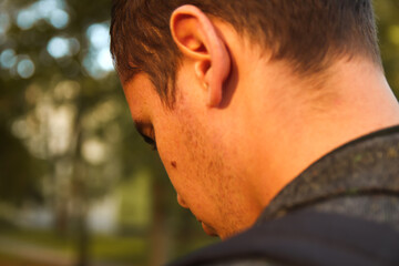 Defocus closeup portrait of a young handsome man sad looking down in the park, the woods in autumn. Portrait on the nature of the park, the woods, on the street. Sad. Out of focus