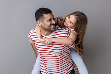 Joyful father giving piggyback ride for his charming daughter, smiling girl looking at her daddy...
