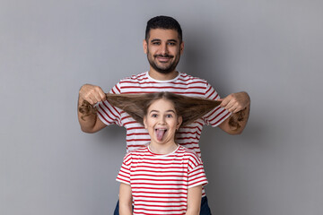 Portrait of happy funny father and daughter having fun, cute kid showing tongue out, dad pulling...
