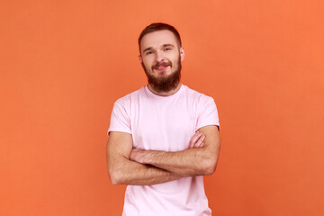 Portrait of bearded man standing with crossed arms, looking at camera, expressing positive...