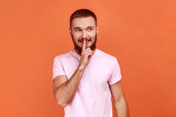 Portrait of positive bearded man showing hush with finger on his lips gesture, shushing, asking to...